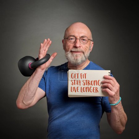 Foto de Get fit, stay strong, live longer - motivational note held by a senior man exercising with a kettlebell - Imagen libre de derechos