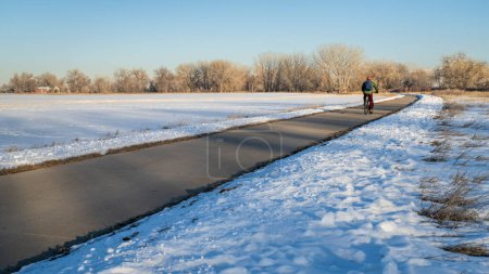 Téléchargez les photos : Cycliste masculin se déplaçant sur une piste cyclable dans les paysages d'hiver - Poudre River Trail dans le nord du Colorado entre WIndsor et Greeley - en image libre de droit
