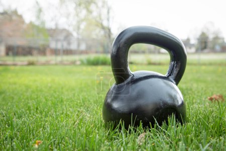Foto de Kettlebell negro de hierro pesado sobre hierba verde en el patio trasero - concepto de fitness al aire libre - Imagen libre de derechos