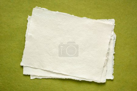 Foto de Hoja pequeña de papel blanco Khadi en blanco contra papel de trapo verde - Imagen libre de derechos