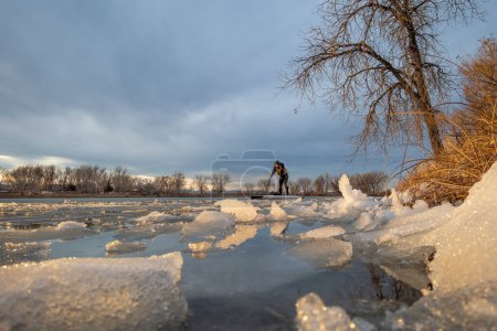 Foto de Macho mayor en stand up paddleboard en un lago con hielo flotante al atardecer en invierno o principios de primavera en Colorado - Imagen libre de derechos