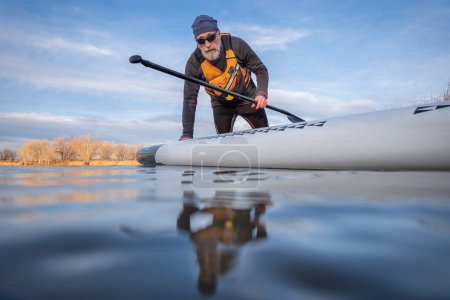 Photo for Senior paddler and his paddleboard on lake in winter or early spring in Colorado, frog perspective (partially submerged action camera) - Royalty Free Image