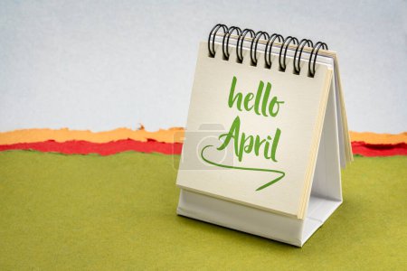 Foto de Hola abril - nota en un pequeño calendario de escritorio contra el paisaje abstracto de papel - Imagen libre de derechos