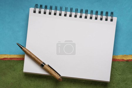 Téléchargez les photos : Carnet de croquis en spirale vierge avec pages blanches avec un stylo contre paysage abstrait coloré - en image libre de droit