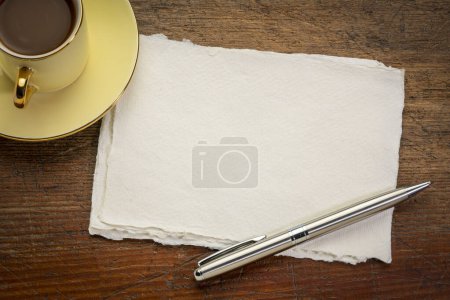Foto de Pequeña hoja de papel de trapo blanco Khadi en blanco sobre mesa de madera rústica con café - Imagen libre de derechos