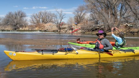 Téléchargez les photos : Evans, CO, États-Unis - 1er avril 2023 : Les kayakistes se reposent et tournent des photos sur un banc de sable après le portage du barrage lors d'un voyage de pagaie printanier sur la rivière South Platte. - en image libre de droit