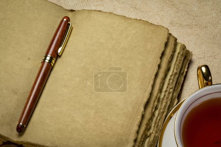 Foto de Diario de cuero retro en blanco con páginas de papel hechas a mano de borde adornado con un bolígrafo elegante y una taza de té, concepto de diario - Imagen libre de derechos