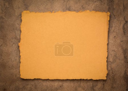 Foto de Naranja y marrón abstracto - una hoja de papel de trapo indio en blanco contra papel de corteza texturizado, espacio de copia - Imagen libre de derechos