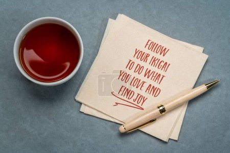 Foto de Seguir su ikigai - para hacer lo que amas y encontrar la alegría - escritura inspiradora en una servilleta con té, concepto japonés de un propósito de vida - Imagen libre de derechos