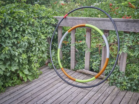Téléchargez les photos : Weighted hula hoop and one home made from a sprinkler pipe on a wooden backyard deck in summer scenery, core workout concept - en image libre de droit