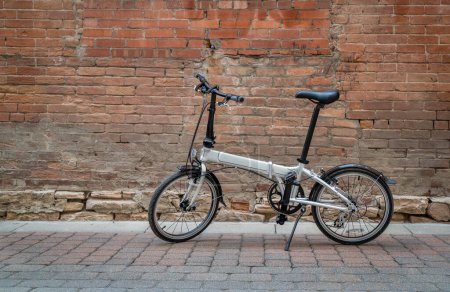 Téléchargez les photos : Vélo pliant léger dans une allée contre un mur de briques grunge - en image libre de droit