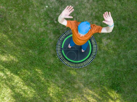 Téléchargez les photos : Senior homme en surpoids faisant de l'exercice sur un mini trampoline dans sa cour arrière, concept de remise en forme et de rebond, vue aérienne - en image libre de droit