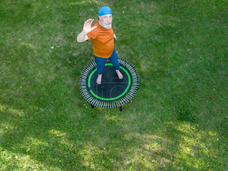 Photo for Senior overweight male exercising on a mini trampoline in his backyard backyard, fitness and rebounding concept, aerial view - Royalty Free Image
