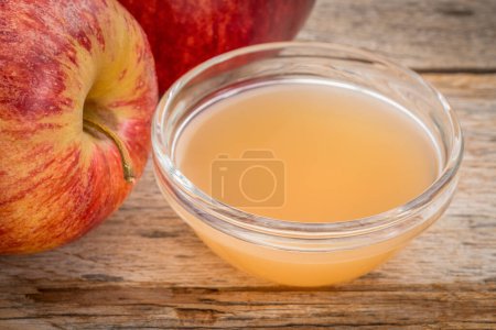 ungefilterter, roher Apfelessig mit Mutter - eine kleine Glasschale mit frischen roten Äpfeln