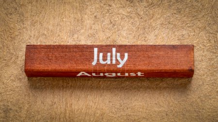 Téléchargez les photos : Texte de juillet et août sur bloc de bois contre papier d'écorce fait à la main dans des tons de terre, concept de calendrier - en image libre de droit