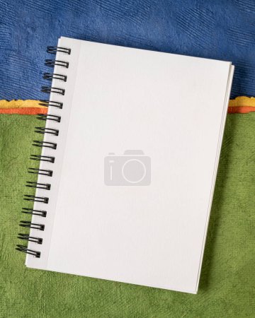 Photo for Blank spiral sketchbook with white pages against colorful abstract paper landscape - Royalty Free Image