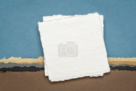 Foto de Pequeña hoja de papel de trapo blanco Khadi en blanco de la India contra el paisaje abstracto en tonos pastel tierra - Imagen libre de derechos
