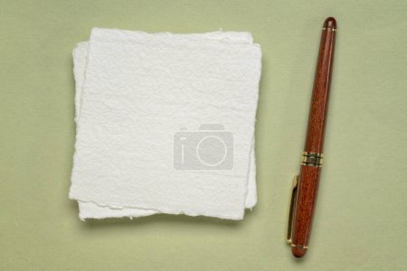 Foto de Pequeña hoja de papel de trapo blanco Khadi en blanco con una pluma de madera de lujo sobre fondo verde pastel - Imagen libre de derechos