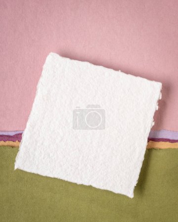 Foto de Pequeña hoja de papel de trapo blanco Khadi en blanco de la India contra el paisaje abstracto en tonos pastel rosa y verde - Imagen libre de derechos