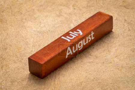 Téléchargez les photos : Texte de juillet et août sur bloc de bois contre papier d'écorce fait à la main dans des tons de terre, concept de calendrier - en image libre de droit