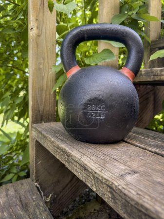 Photo for Heavy iron competition kettlebell for weight training on wooden rustic stairs in backyard, home gym and fitness concept - Royalty Free Image