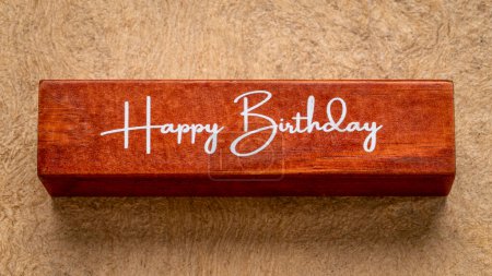 Téléchargez les photos : Texte de joyeux anniversaire sur bloc de bois contre papier d'écorce fait à la main dans des tons de terre, concept de salutation - en image libre de droit