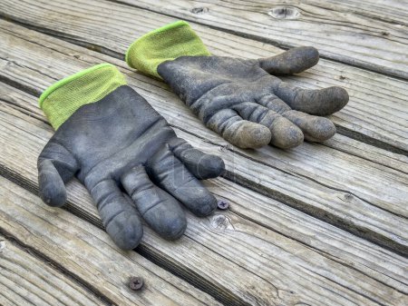 Foto de Un par de guantes de jardín de bambú bien utilizados y sucios en una cubierta rústica de madera - Imagen libre de derechos