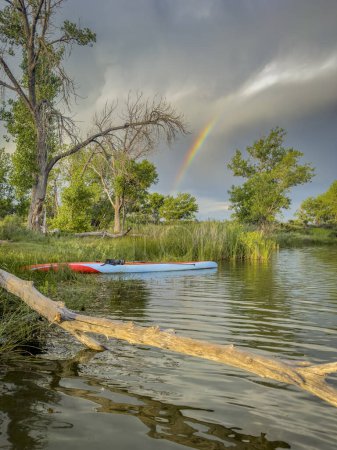 Photo for Long and narrow racing stand up paddleboard at lake shore, stormy sky with rainbow - Royalty Free Image