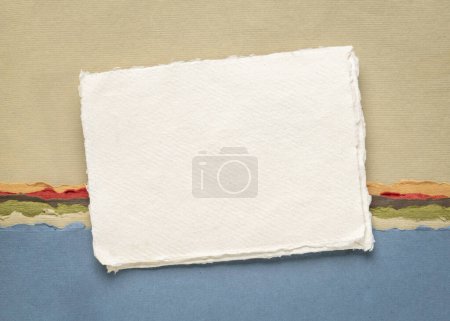 Foto de Pequeña hoja de blanco blanco papel de trapo Khadi de la India contra el paisaje abstracto en la tierra y tonos azules - Imagen libre de derechos