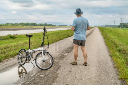 Photo for Senior athletic man with a folding bike - biking on a levee trail along Chain of Rocks Canal near Granite City in Illinois - Royalty Free Image