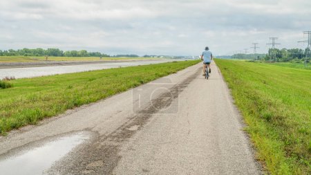 Photo for Senior athletic man is riding a folding bike - biking on a levee trail along Chain of Rocks Canal near Granite City in Illinois - Royalty Free Image