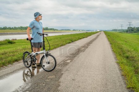 Photo for Senior athletic man is riding a folding bike - biking on a levee trail along Chain of Rocks Canal near Granite City in Illinois - Royalty Free Image