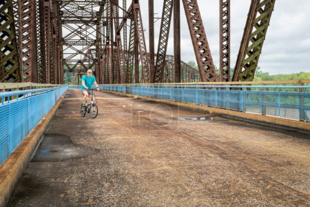 Foto de Hombre atlético senior con una bicicleta plegable - andar en bicicleta en un histórico Puente de la Cadena de Roca sobre el Río Mississippi por encima de St Louis - Imagen libre de derechos