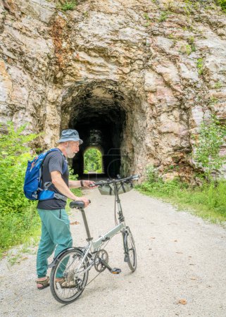 Photo for Senior man with a folding bike on Katy Trail at a tunnel near Rocheport, Missouri, summer scenery. The Katy Trail is 237 mile bike trail converted from an old railroad. - Royalty Free Image