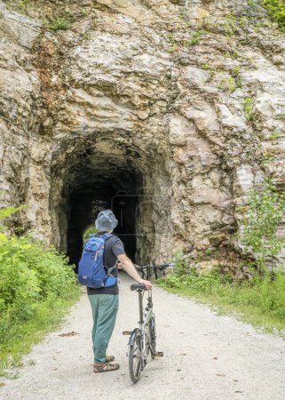 Téléchargez les photos : Homme âgé avec un vélo pliant sur Katy Trail dans un tunnel près de Rocheport, Missouri, paysages d'été. Le sentier Katy est un sentier cyclable de 237 milles converti d'un ancien chemin de fer. - en image libre de droit