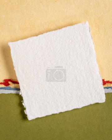 Foto de Pequeña hoja de papel de trapo blanco Khadi en blanco de la India contra el paisaje abstracto en tonos pastel amarillo y verde - Imagen libre de derechos