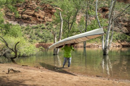 Téléchargez les photos : Senior male is portaging a decked expedition canoe at foothills of northern Colorado in spring scenery - en image libre de droit