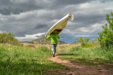 Téléchargez les photos : Senior male is portaging a decked expedition canoe at foothills of northern Colorado in spring scenery - en image libre de droit