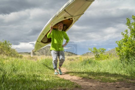 Photo for Senior male is portaging a decked expedition canoe at foothills of northern Colorado in spring scenery - Royalty Free Image
