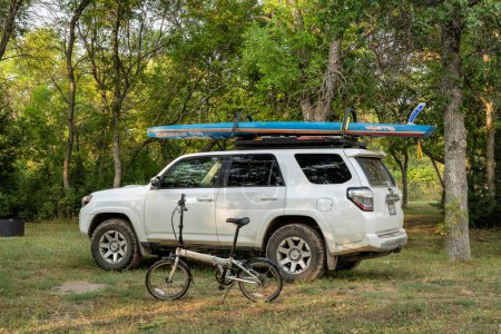 Foto de Halsey, NE, Estados Unidos - 9 de septiembre de 2023: Dahon Mariner bicicleta plegable y Toyota 4Runner SUV con un stand up paddleboard de carreras en los portaequipajes de un camping en Nebraska National Forest. - Imagen libre de derechos