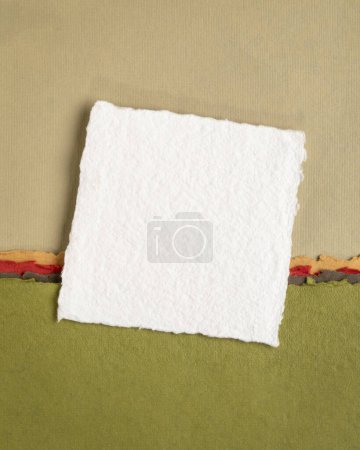Téléchargez les photos : Petite feuille de papier blanc blanc blanc Khadi de l'Inde contre paysage abstrait dans des tons pastel rose et vert - en image libre de droit