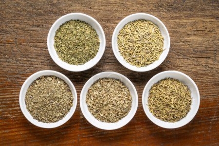 Photo for Herb spices - dried leaves of parsley, rosemary, thyme, oregano and basil, collection of small ceramic bowls on a rustic wood, top view - Royalty Free Image