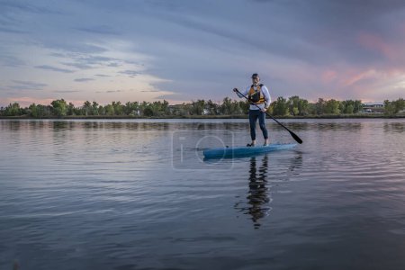 Photo for Lonely stand up paddler on a lake in Colorado at dusk with dramatic sunset clouds - Royalty Free Image