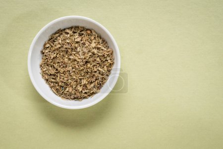 Photo for Oregano dried herb - small ceramic bowl on textured paper with a copy space, top view - Royalty Free Image