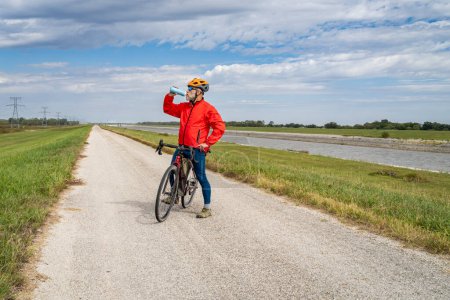 Téléchargez les photos : Homme sportif senior boit de l'eau pendant le vélo un vélo de randonnée en gravier sur un sentier de levée le long de la chaîne de Rocks Canal près de Granite City dans l'Illinois - en image libre de droit