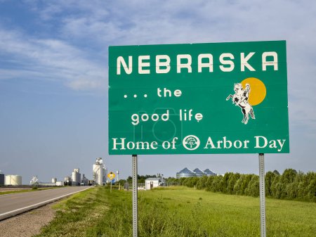 Foto de Nebraska, la buena vida, hogar del Día del Árbol - señal de bienvenida al borde de la carretera en la frontera estatal con Colorado, paisaje de verano con una ciudad rural en el fondo - Imagen libre de derechos