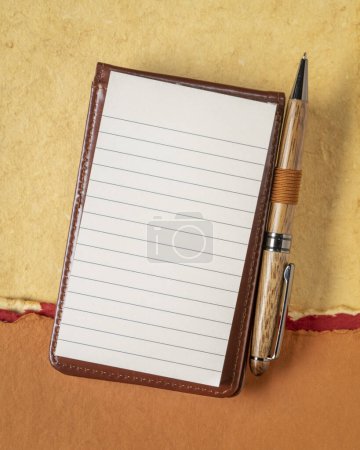 Photo for Blank sheet of ruled paper in a small journal with a luxury pen against textured art paper - Royalty Free Image