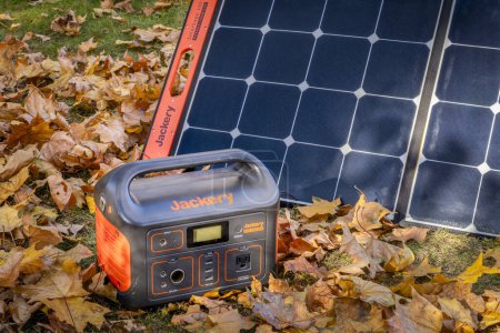 Photo for Fort Collins, CO, USA - November 5, 2023: Jackery Explorer 500, 518Wh lithium Portable Power Station, is being charged by a solar panel in a field covered by maple dry leaves. - Royalty Free Image