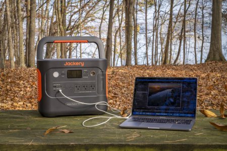 Foto de Colbert Ferry Park, AL, Estados Unidos - 23 de noviembre de 2023: Jackery Explorer 1000 Plus Portable Power Station está cargando el portátil MacBook Pro en una mesa de picnic a orillas del río Tennessee. - Imagen libre de derechos