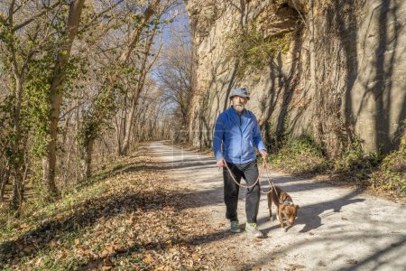 Foto de Hombre mayor está caminando con un perro pitbull en Katy Trail cerca de Rocheport, Missouri, a finales de noviembre paisaje forestal - Imagen libre de derechos